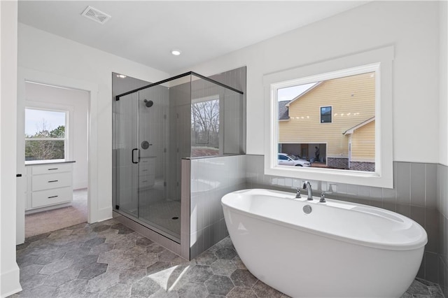 full bath featuring visible vents, a wainscoted wall, a stall shower, a soaking tub, and tile walls