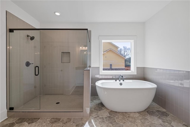 full bathroom with a soaking tub, a stall shower, tile walls, and a wainscoted wall