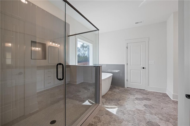 bathroom featuring visible vents, a stall shower, tile walls, wainscoting, and a soaking tub