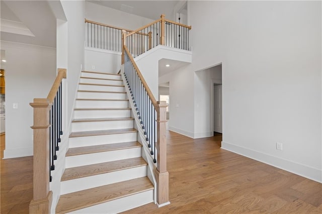 stairs featuring wood finished floors, baseboards, and a towering ceiling