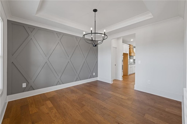 unfurnished room with crown molding, a raised ceiling, an inviting chandelier, and wood finished floors