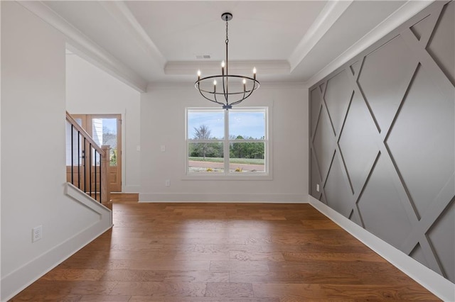 unfurnished dining area with wood finished floors, baseboards, a raised ceiling, a chandelier, and stairs