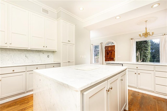 kitchen featuring decorative backsplash, light stone counters, wood-type flooring, decorative light fixtures, and a kitchen island