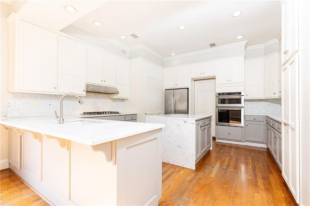 kitchen with a breakfast bar, kitchen peninsula, appliances with stainless steel finishes, tasteful backsplash, and white cabinetry