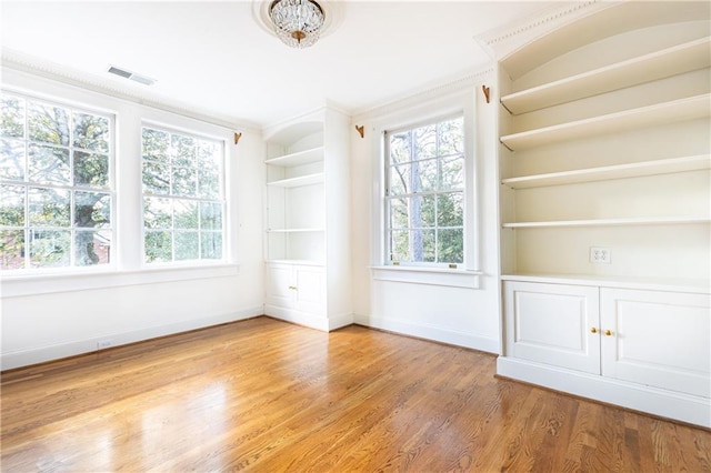 unfurnished room with built in shelves, light hardwood / wood-style flooring, and crown molding