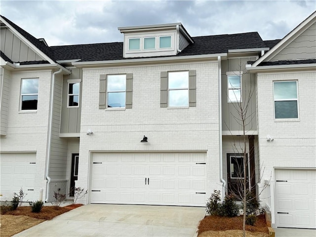 townhome / multi-family property with driveway, a garage, a shingled roof, board and batten siding, and brick siding