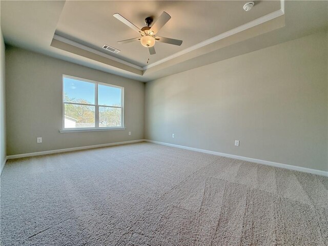 spare room featuring carpet flooring, visible vents, baseboards, a raised ceiling, and crown molding