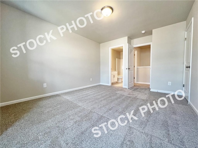 unfurnished bedroom featuring lofted ceiling, carpet flooring, baseboards, and ensuite bathroom