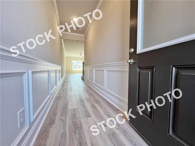 hallway with a decorative wall, wainscoting, wood finished floors, and crown molding