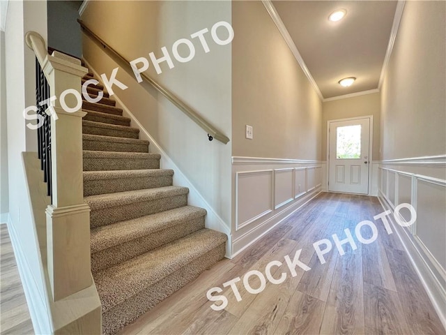 stairway featuring a wainscoted wall, ornamental molding, a decorative wall, and wood finished floors