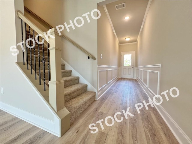 staircase with visible vents, a wainscoted wall, ornamental molding, wood finished floors, and a decorative wall