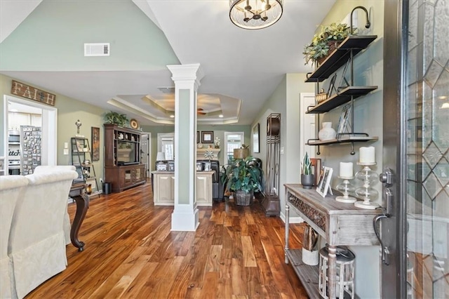 foyer entrance with dark wood-type flooring, a tray ceiling, and ornate columns