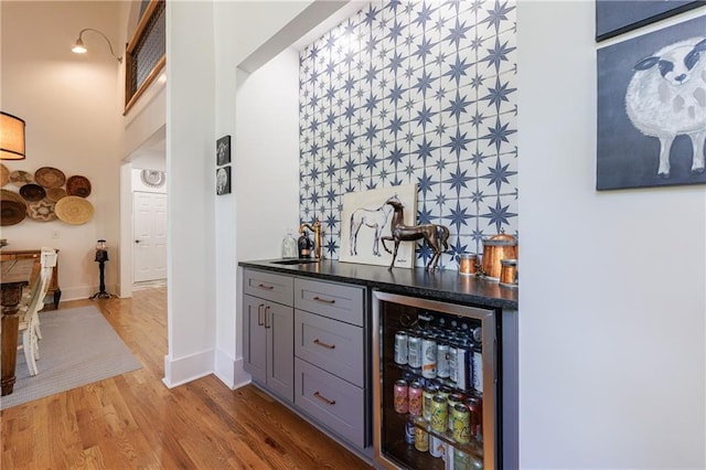 bar featuring a sink, wine cooler, bar area, baseboards, and wood finished floors