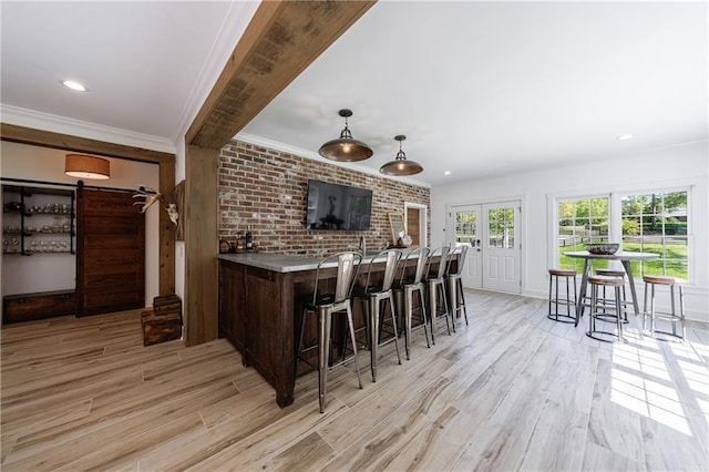 bar with ornamental molding, light wood finished floors, brick wall, and pendant lighting