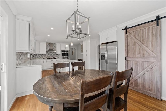 dining space featuring a notable chandelier, a barn door, sink, and light wood-type flooring