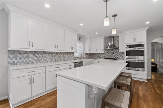 kitchen featuring a kitchen island, double oven, white cabinetry, dishwasher, and wall chimney exhaust hood