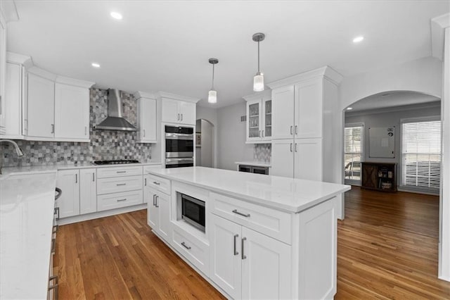 kitchen featuring a kitchen island, pendant lighting, white cabinets, stainless steel appliances, and wall chimney range hood