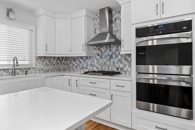 kitchen with white cabinetry, stainless steel appliances, sink, and wall chimney range hood