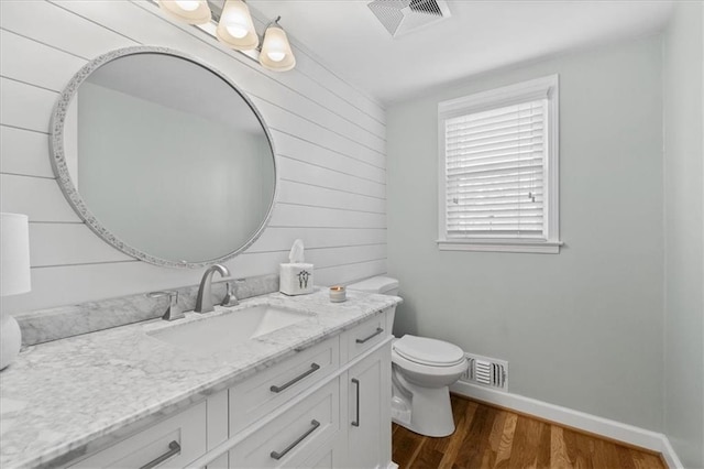 bathroom with hardwood / wood-style flooring, vanity, toilet, and wood walls