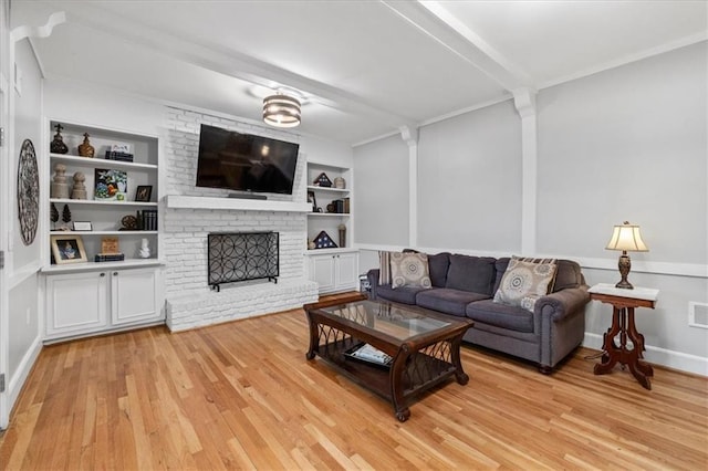 living room with built in shelves, a brick fireplace, light hardwood / wood-style flooring, ornamental molding, and beam ceiling