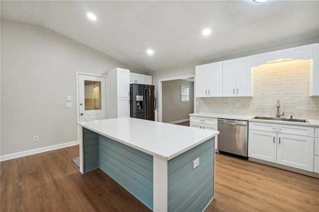kitchen with stainless steel dishwasher, vaulted ceiling, a sink, black fridge, and white cabinetry