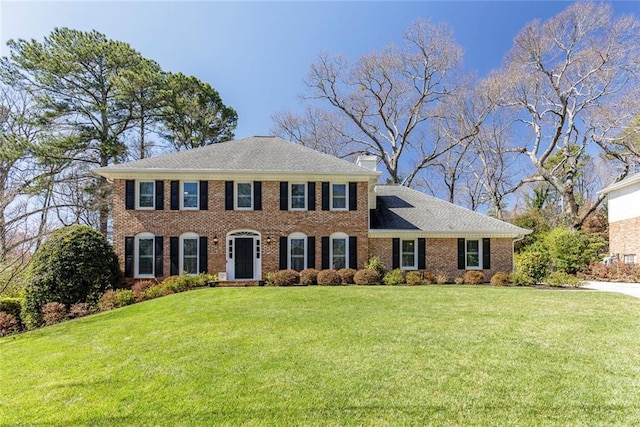 colonial-style house featuring brick siding, a chimney, and a front lawn