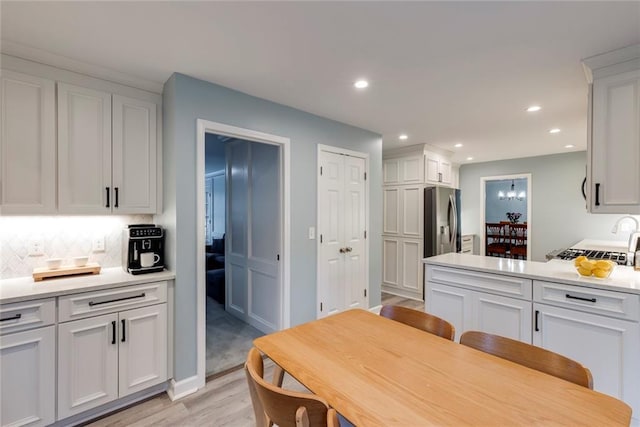 kitchen with light wood-type flooring, recessed lighting, decorative backsplash, white cabinets, and stainless steel fridge