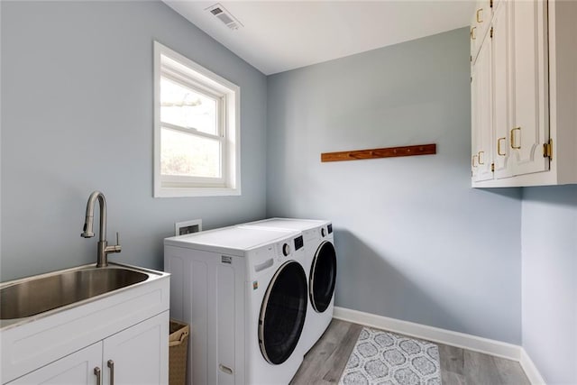 clothes washing area with baseboards, light wood-style flooring, separate washer and dryer, cabinet space, and a sink