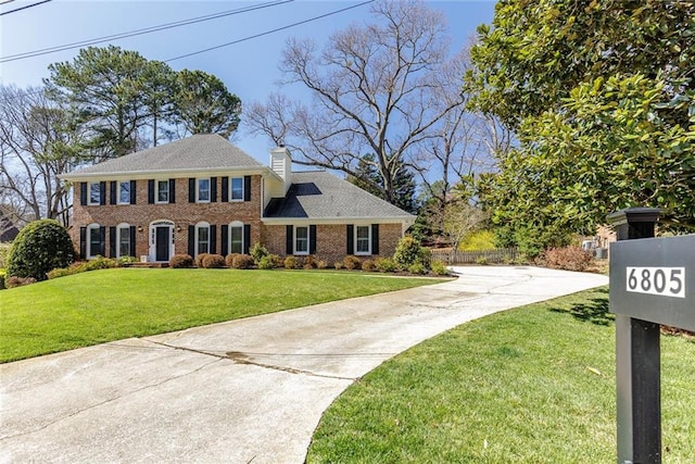 view of front facade featuring fence, concrete driveway, a front yard, brick siding, and a chimney