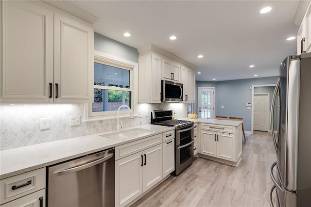 kitchen featuring light wood-type flooring, a sink, stainless steel appliances, a peninsula, and light countertops