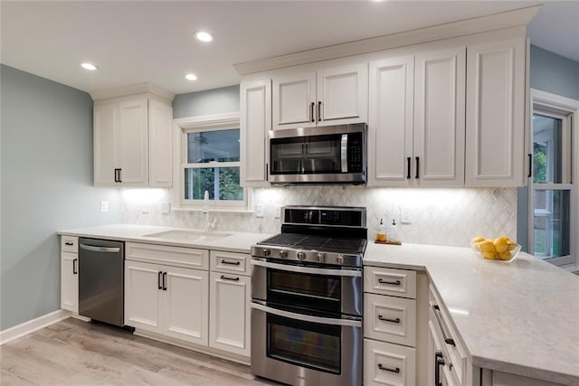 kitchen featuring a sink, backsplash, stainless steel appliances, light wood-style floors, and light countertops