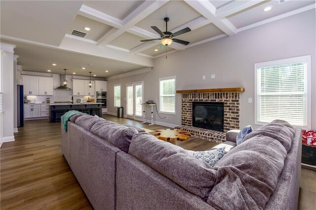 living room featuring dark hardwood / wood-style floors, a brick fireplace, a wealth of natural light, and coffered ceiling
