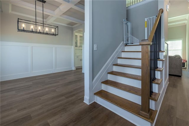 stairway featuring an inviting chandelier, wood-type flooring, beam ceiling, and coffered ceiling
