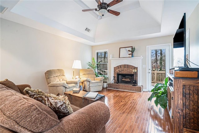 living room with hardwood / wood-style floors, a fireplace, a raised ceiling, and ceiling fan