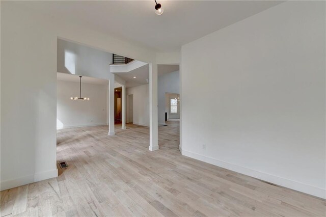 unfurnished living room featuring french doors, a towering ceiling, a chandelier, and light wood-type flooring