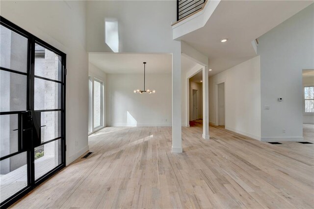 unfurnished living room featuring an inviting chandelier, a towering ceiling, and light hardwood / wood-style floors