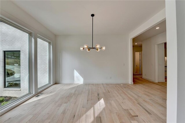 unfurnished living room featuring an inviting chandelier and light hardwood / wood-style flooring