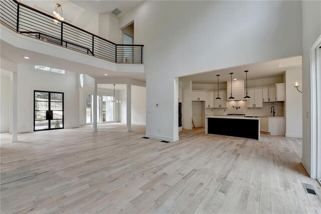 unfurnished living room featuring a towering ceiling, an inviting chandelier, and light hardwood / wood-style floors