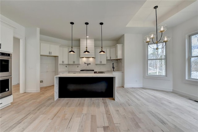 kitchen with sink, decorative backsplash, white cabinets, a kitchen island, and decorative light fixtures