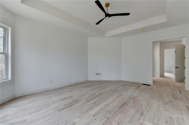 empty room featuring ceiling fan, a raised ceiling, and light hardwood / wood-style flooring