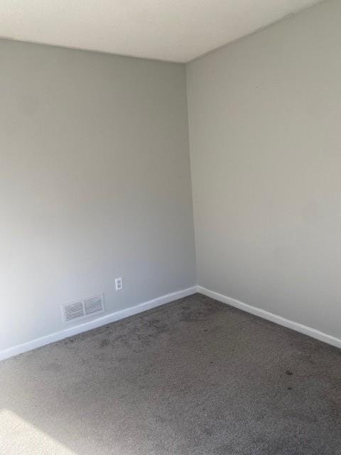 unfurnished room with visible vents, dark carpet, and baseboards
