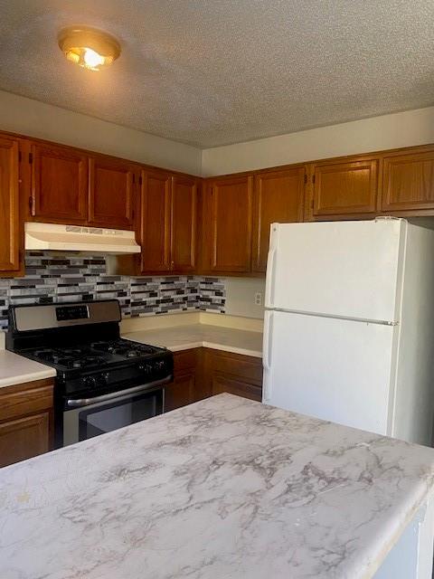 kitchen with gas range, brown cabinetry, freestanding refrigerator, and under cabinet range hood
