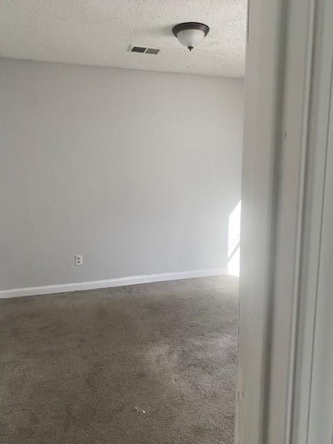 unfurnished room with visible vents, baseboards, a textured ceiling, and dark carpet