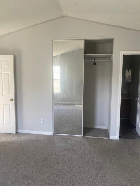 unfurnished bedroom featuring a closet, baseboards, lofted ceiling, and carpet