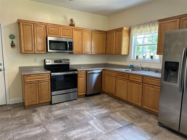 kitchen with dark countertops, appliances with stainless steel finishes, a sink, brown cabinetry, and stone finish floor