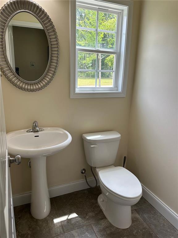 half bath with toilet, baseboards, a sink, and a healthy amount of sunlight