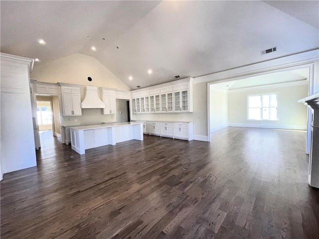 unfurnished living room featuring dark wood-type flooring, ornamental molding, and high vaulted ceiling