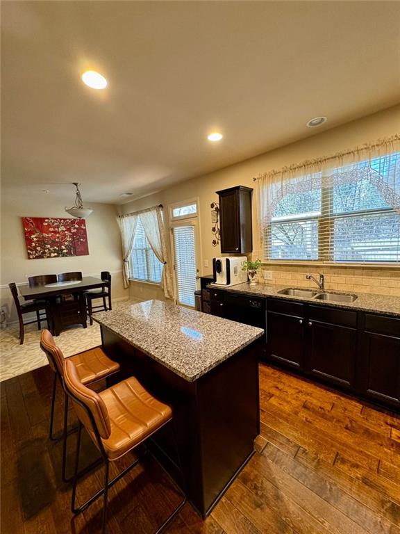 kitchen with dark wood-type flooring, a sink, light stone countertops, and a center island