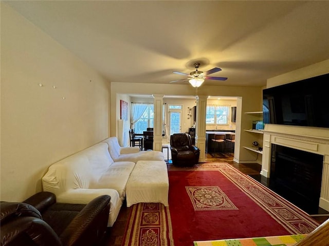 living area featuring a ceiling fan, a fireplace, ornate columns, and wood finished floors