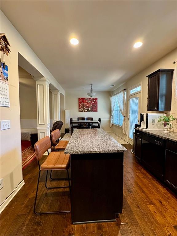 kitchen featuring light stone counters, a kitchen island, open floor plan, dark wood-style floors, and decorative columns